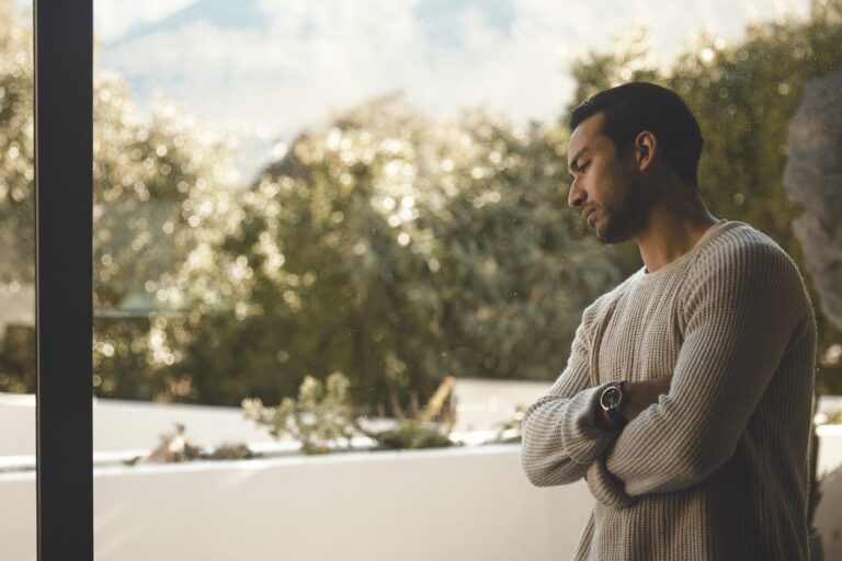 A young man going through depression, standing at the window in thought