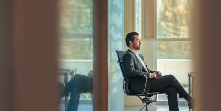 Businessman sitting in chair with eyes closed practicing mindfulness and relaxing in business office space alone