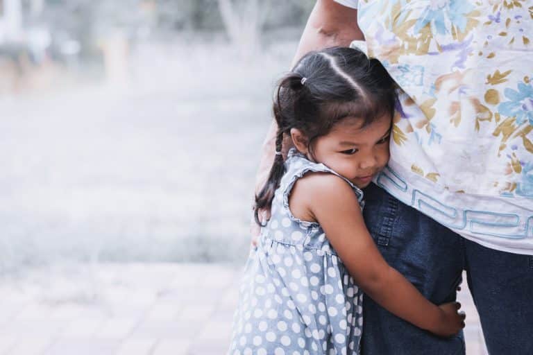 Little girl with childhood anxiety holding on to her father's leg