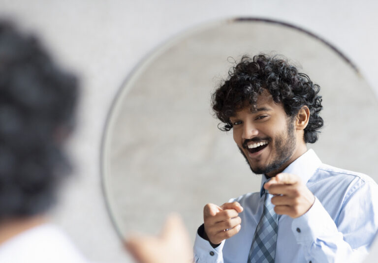 Young man smiling in mirror after repeating daily positive affirmations
