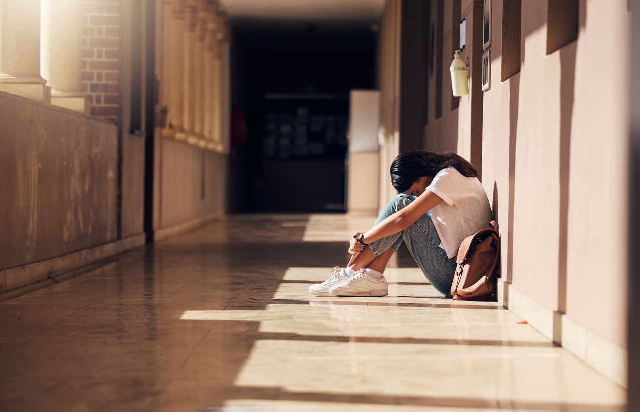 Lonely girl sitting in the school hallway showing warning signs of suicide