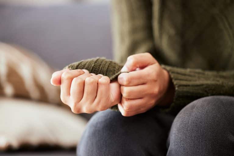 A shot of unrecognizable hands of someone on the couch who might be considering self-harm