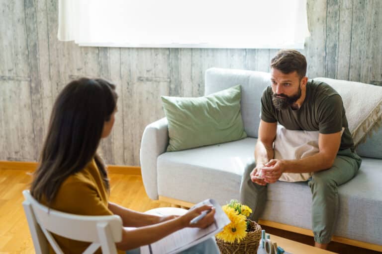 Man having a therapy session, talking with a psychologist in a comfortable office about trauma.