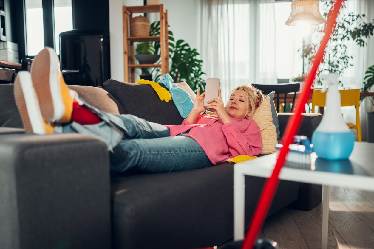Young woman taknig a break from her chores, looking at her phone and procrastinating